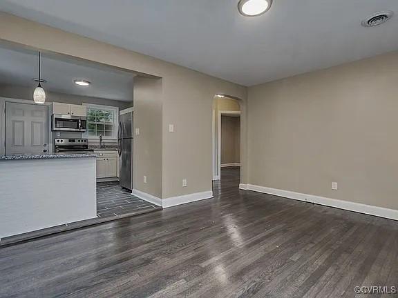 unfurnished living room featuring arched walkways, dark wood-style floors, visible vents, and baseboards