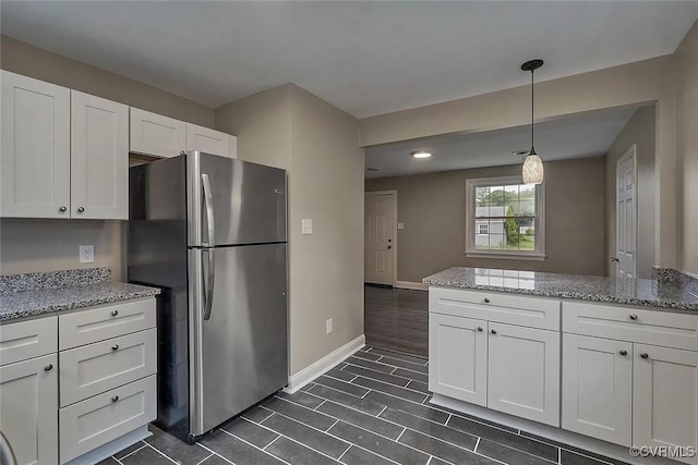 kitchen featuring baseboards, white cabinets, freestanding refrigerator, light stone countertops, and pendant lighting