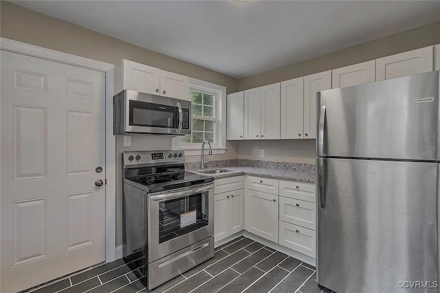 kitchen featuring appliances with stainless steel finishes, a sink, light stone countertops, and white cabinets