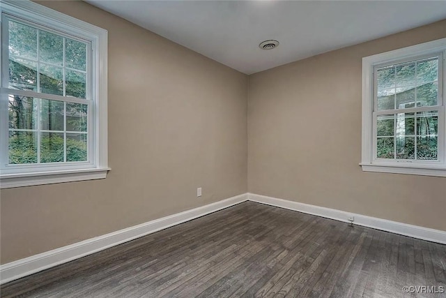 empty room featuring visible vents, dark wood finished floors, and baseboards