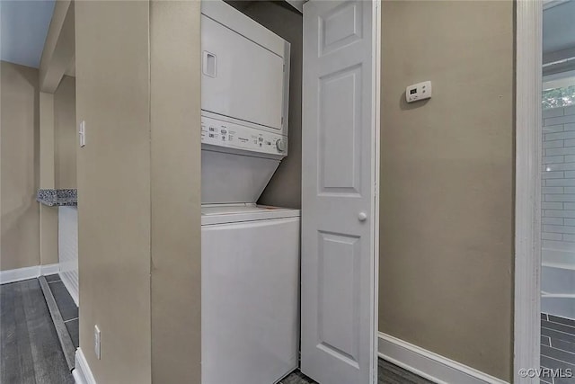 laundry area featuring stacked washer / dryer, laundry area, baseboards, and dark wood-style flooring