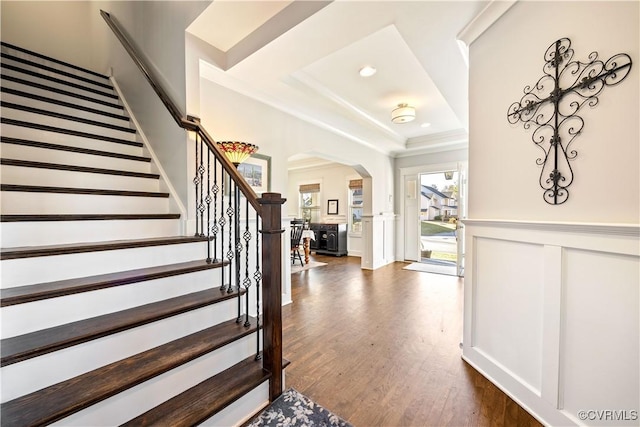 foyer entrance with arched walkways, a tray ceiling, a wainscoted wall, a decorative wall, and dark wood-type flooring