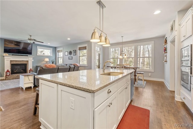 kitchen with appliances with stainless steel finishes, a brick fireplace, a sink, and dark wood-style floors