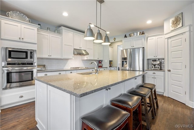 kitchen with under cabinet range hood, a sink, white cabinets, appliances with stainless steel finishes, and decorative backsplash