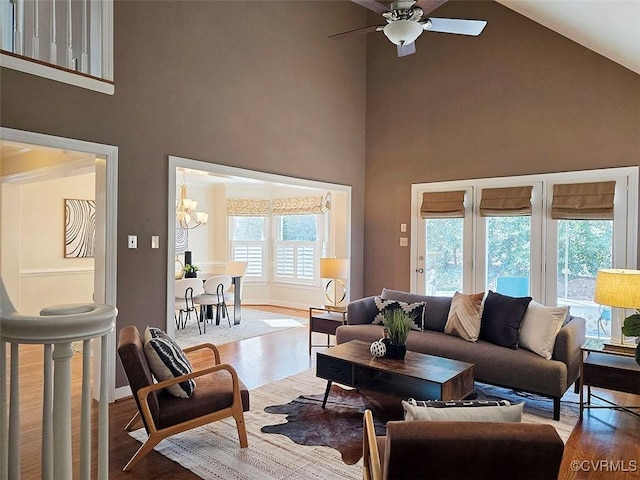 living room with baseboards, high vaulted ceiling, wood finished floors, and ceiling fan with notable chandelier