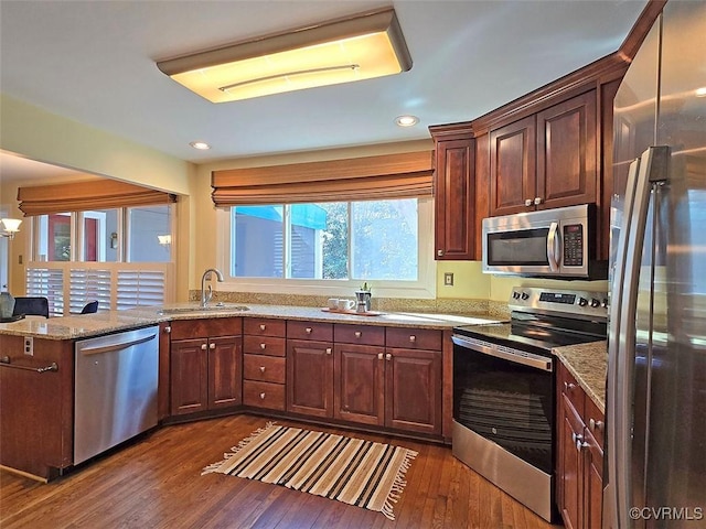 kitchen with light stone counters, a peninsula, a sink, appliances with stainless steel finishes, and dark wood finished floors