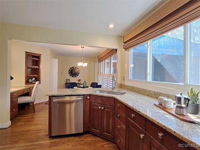 kitchen with light stone counters, a peninsula, wood finished floors, a sink, and dishwasher