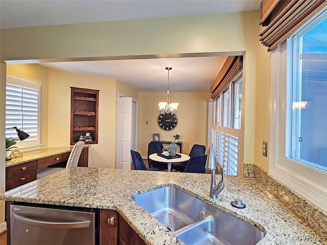 kitchen with a chandelier, light stone counters, a sink, and stainless steel dishwasher