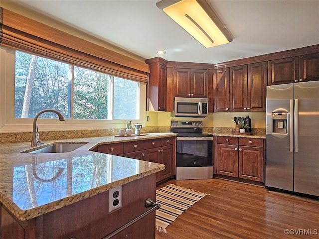 kitchen with stainless steel appliances, dark wood finished floors, a sink, and light stone countertops