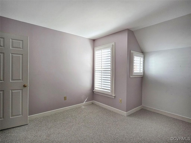 carpeted empty room featuring lofted ceiling and baseboards