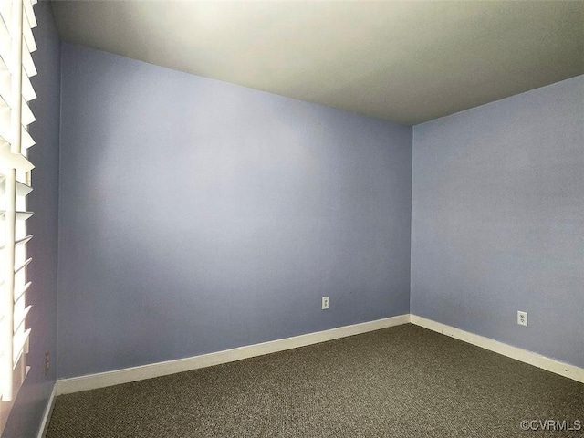 spare room featuring baseboards and dark colored carpet