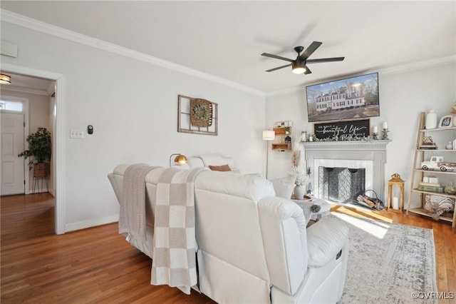 living room featuring ceiling fan, a fireplace with raised hearth, crown molding, and wood finished floors