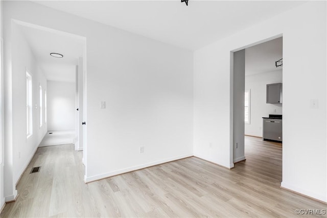 empty room with light wood-style flooring, visible vents, and baseboards