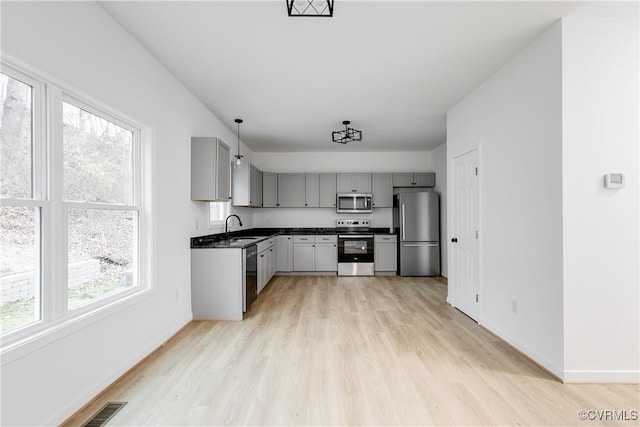 kitchen with a sink, appliances with stainless steel finishes, gray cabinets, light wood finished floors, and dark countertops