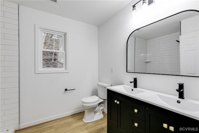 bathroom featuring toilet, double vanity, a sink, and wood finished floors