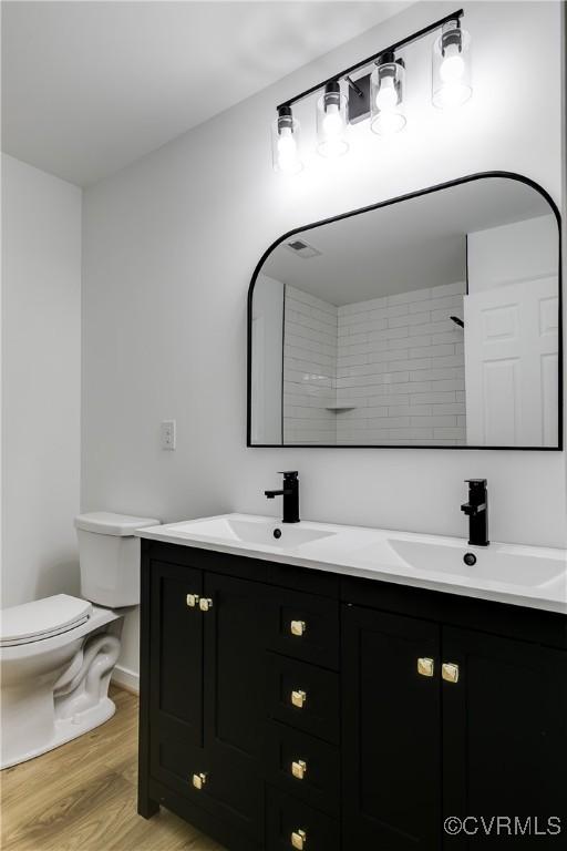 full bath with double vanity, wood finished floors, a sink, and toilet