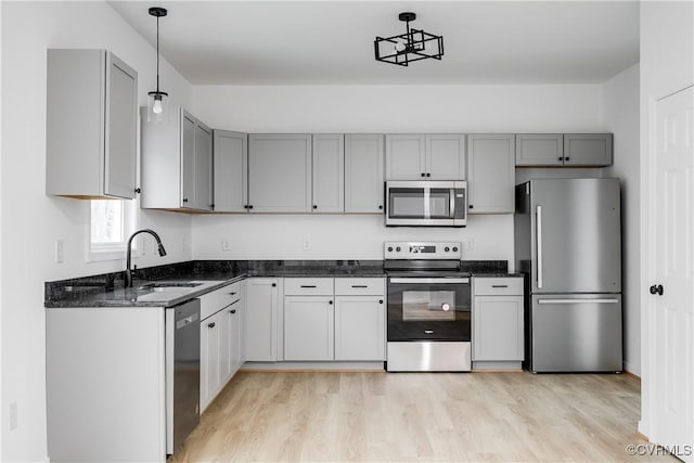 kitchen with stainless steel appliances, a sink, light wood-style floors, gray cabinets, and dark stone countertops