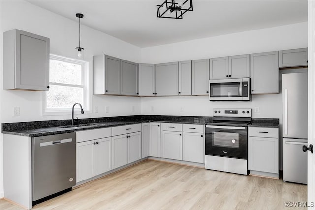 kitchen with stainless steel appliances, gray cabinets, a sink, and light wood-style flooring