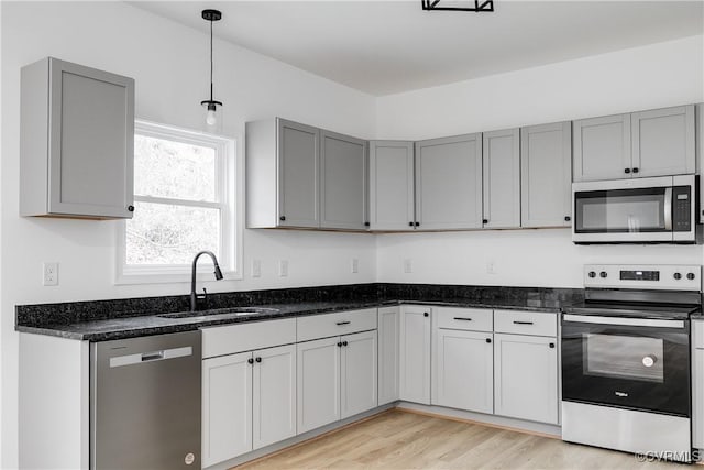 kitchen with appliances with stainless steel finishes, gray cabinets, dark stone countertops, and a sink