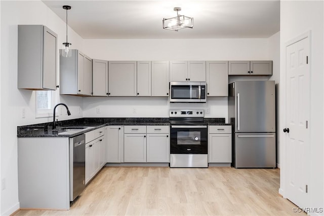 kitchen featuring dark stone counters, light wood-style flooring, stainless steel appliances, gray cabinetry, and pendant lighting