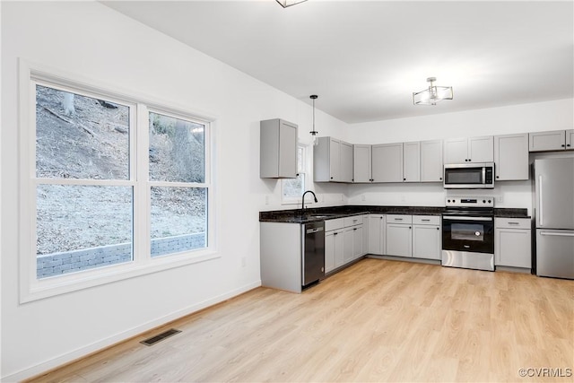 kitchen featuring stainless steel appliances, dark countertops, gray cabinets, visible vents, and light wood-type flooring