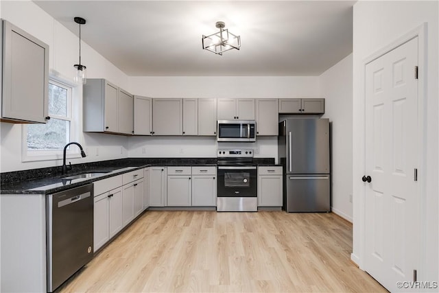 kitchen with stainless steel appliances, a sink, hanging light fixtures, gray cabinets, and light wood finished floors