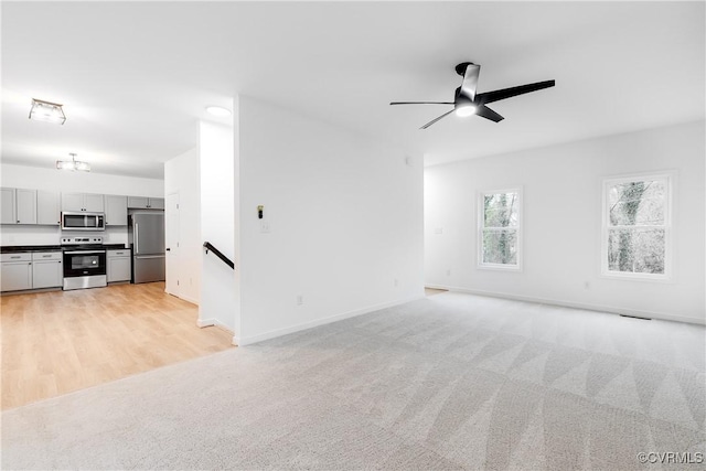 unfurnished living room featuring light carpet, baseboards, and a ceiling fan