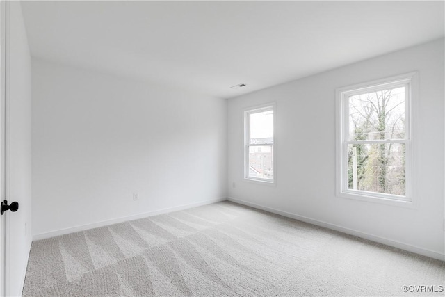 spare room featuring light colored carpet, visible vents, and baseboards