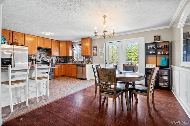 dining area featuring dark wood finished floors, wainscoting, a textured ceiling, crown molding, and a chandelier