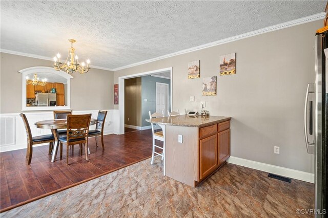 kitchen with brown cabinets, ornamental molding, freestanding refrigerator, stainless steel fridge, and an inviting chandelier