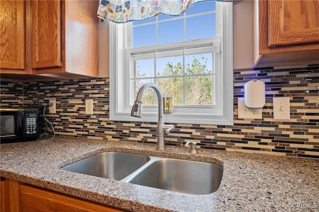 details with decorative backsplash, brown cabinets, light stone countertops, and a sink