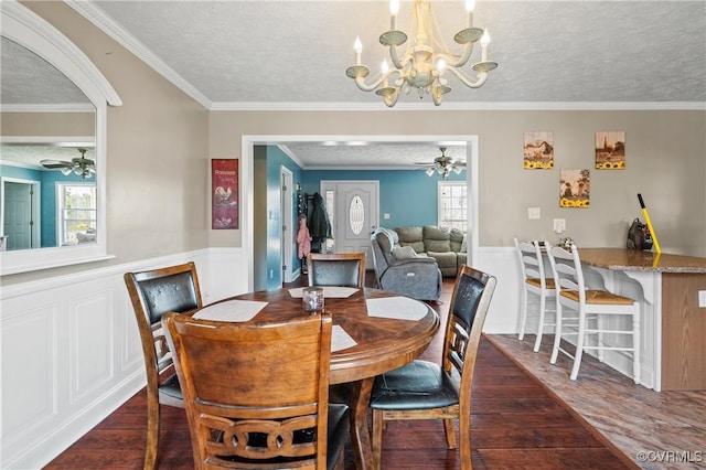 dining space featuring wood finished floors, ceiling fan with notable chandelier, and wainscoting