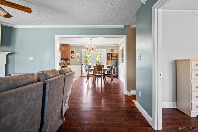 living area featuring ceiling fan with notable chandelier, a textured ceiling, crown molding, and dark wood-style flooring