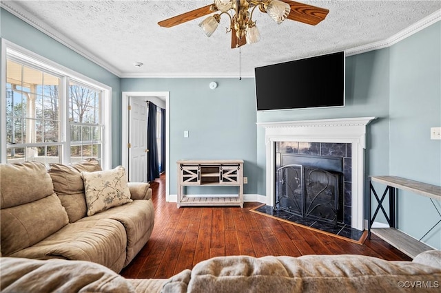 living area with a tile fireplace, crown molding, a ceiling fan, and wood-type flooring