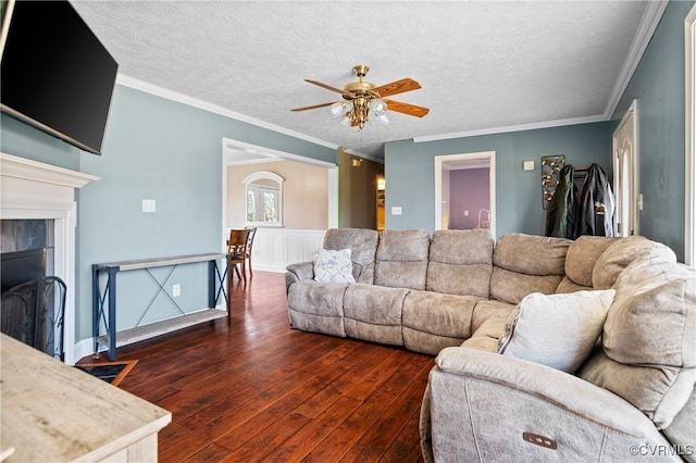 living room with ornamental molding, a ceiling fan, a textured ceiling, wood-type flooring, and a fireplace