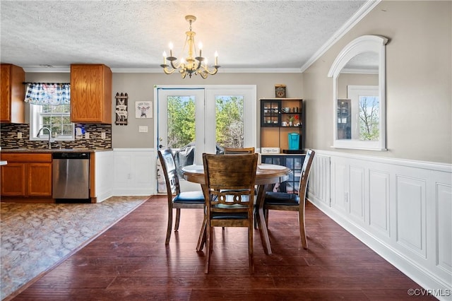 dining area featuring dark wood-type flooring, ornamental molding, wainscoting, a notable chandelier, and a textured ceiling