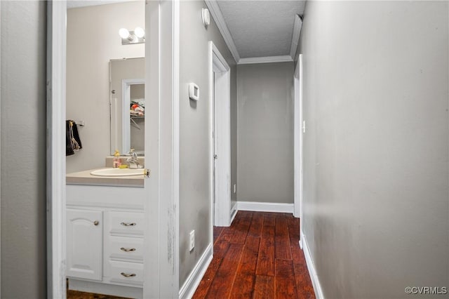 hall with baseboards, dark wood finished floors, a sink, a textured ceiling, and crown molding