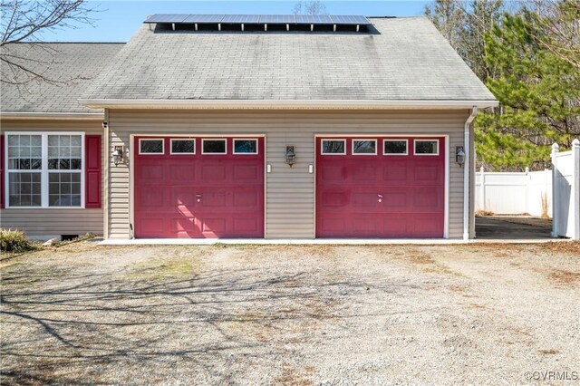 garage featuring roof mounted solar panels, driveway, and fence