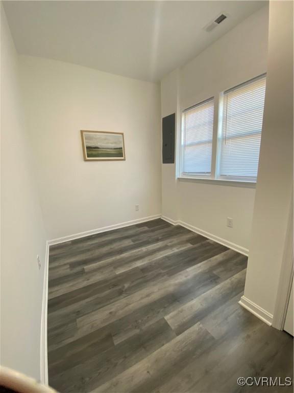 empty room with visible vents, dark wood finished floors, electric panel, and baseboards