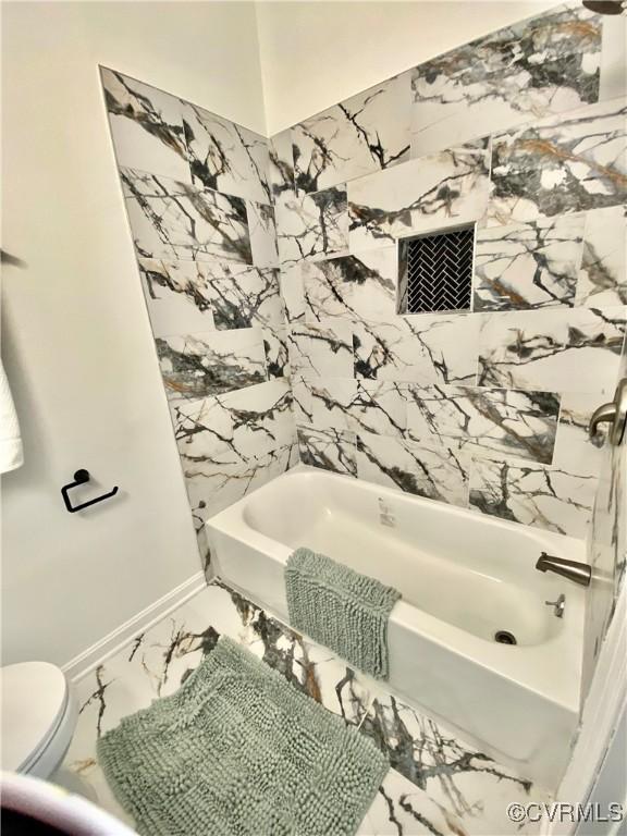 bathroom with toilet, marble finish floor, baseboards, and shower / washtub combination