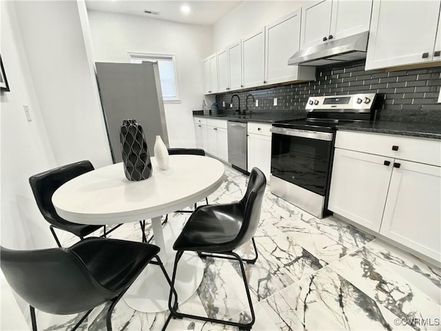 kitchen with marble finish floor, tasteful backsplash, dark countertops, appliances with stainless steel finishes, and under cabinet range hood