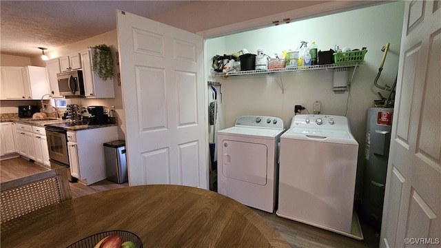 laundry area featuring washing machine and clothes dryer, dark wood finished floors, water heater, laundry area, and a sink