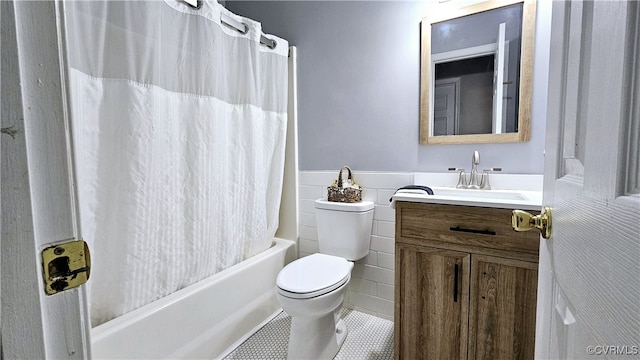 full bath featuring tile patterned flooring, a wainscoted wall, toilet, vanity, and shower / bathtub combination with curtain