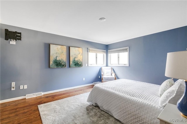 bedroom featuring ornamental molding, visible vents, baseboards, and wood finished floors