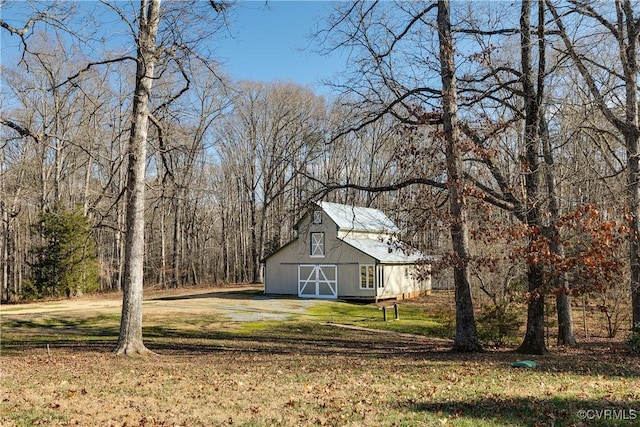 view of front facade featuring a barn, dirt driveway, a forest view, an outdoor structure, and a front yard