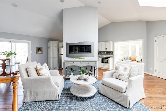 living area with light wood-style floors, lofted ceiling, and baseboards