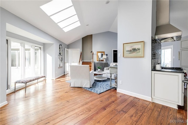 living area with vaulted ceiling with skylight, light wood-style flooring, and baseboards