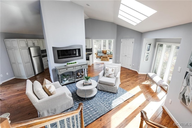 living room with lofted ceiling with skylight, baseboards, and wood finished floors