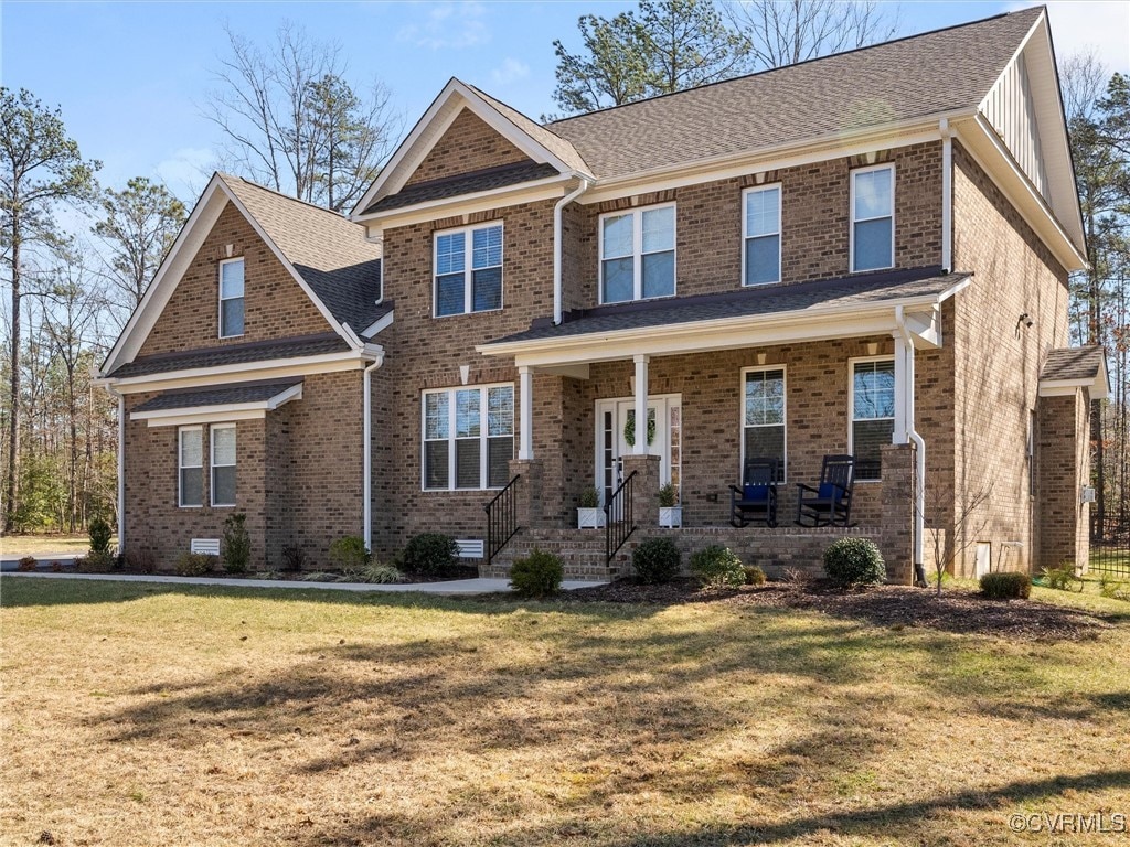 craftsman house featuring covered porch, a front lawn, a shingled roof, and brick siding