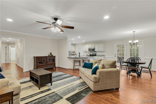 living area with light wood finished floors, baseboards, ornamental molding, ceiling fan with notable chandelier, and recessed lighting